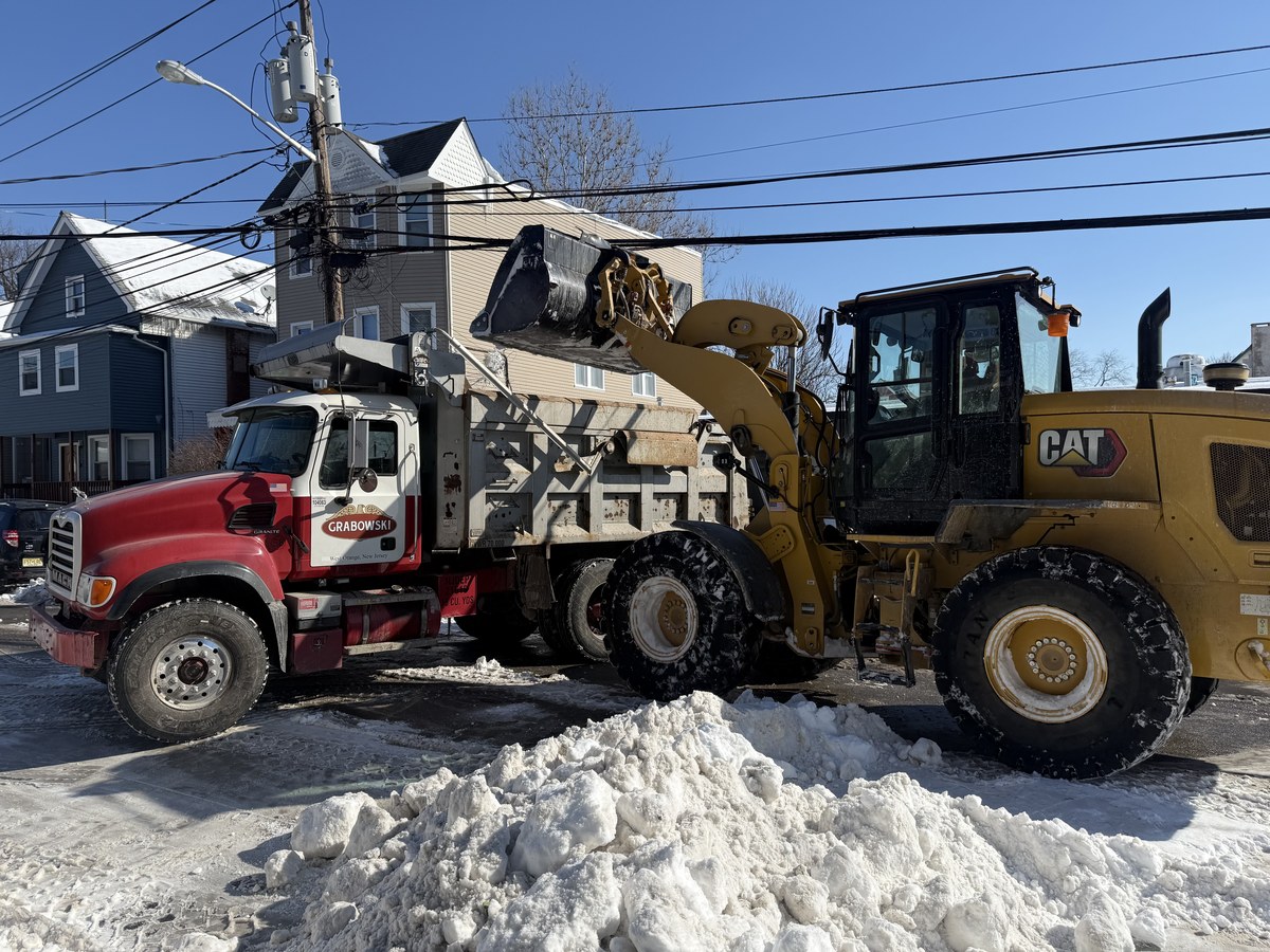 CAT wheel loader scooping snow into a red Grabowski Mack dump truck.
