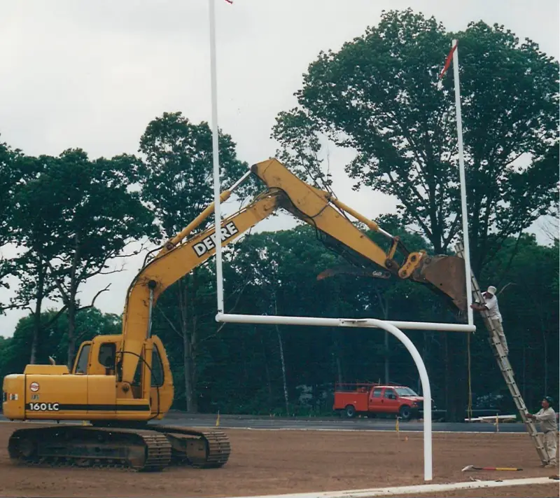 Excavator working a football goalpost during installation.