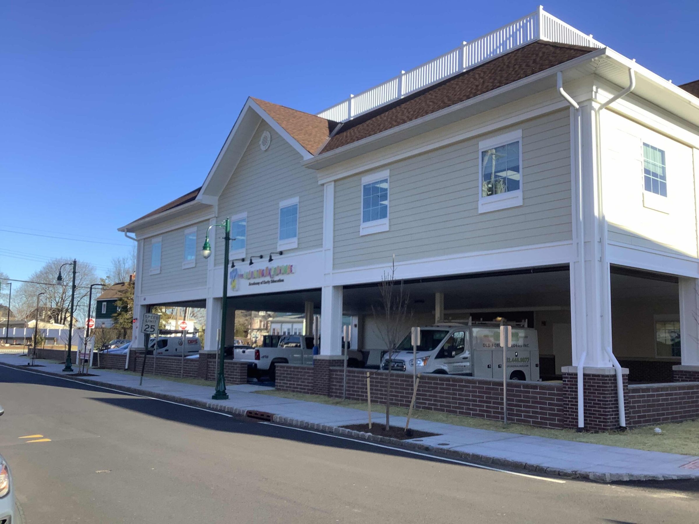 Front exterior of The Learning Experience Summit, NJ location with white clapboard upper, ground-level covered drop-off lane, brick base, branded signage, and street paving in the foreground
