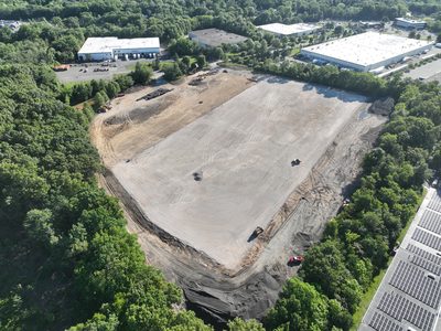 Angled aerial of the Parsippany warehouse pad — dozers grading, neighboring buildings and solar arrays beyond.